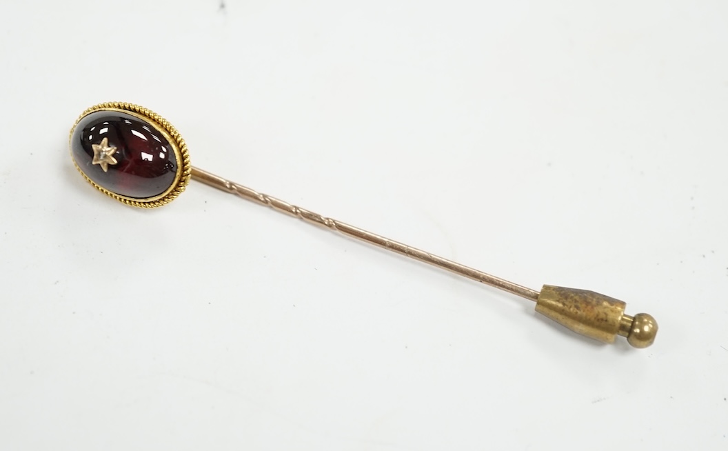 A cased Victorian yellow metal, oval cabochon garnet and diamond chip set stick pin, overall 77mm. Condition - fair